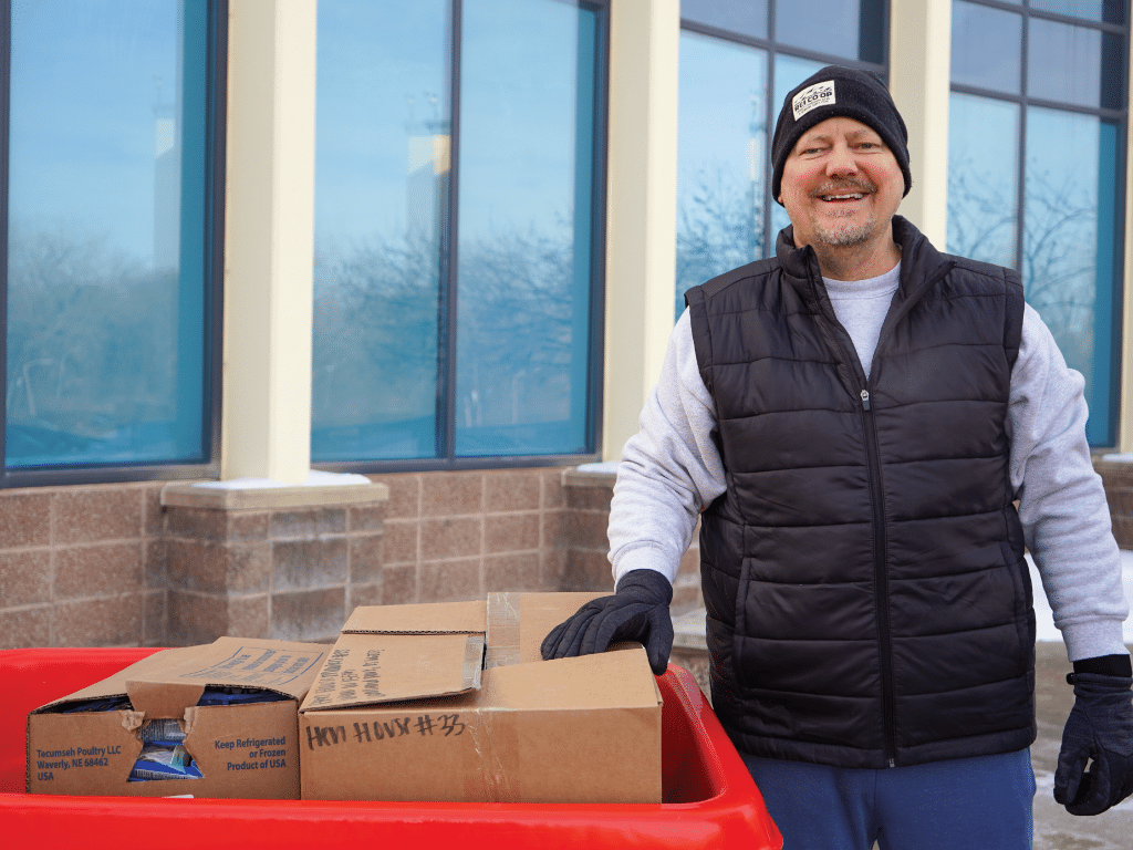 Barrel Buddy volunteer outside of Harvesters in vest, gloves, and hat unloading food into a cart.