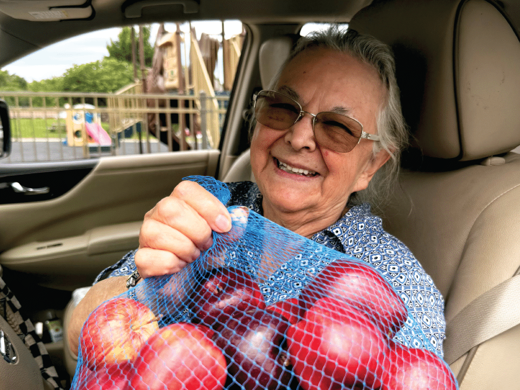 Woman in car with glasses holding a bag of apples she received from a mobile distribution.