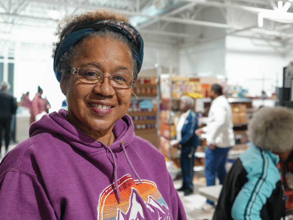 Woman in purple sweatshirt smiling at a food pantry.