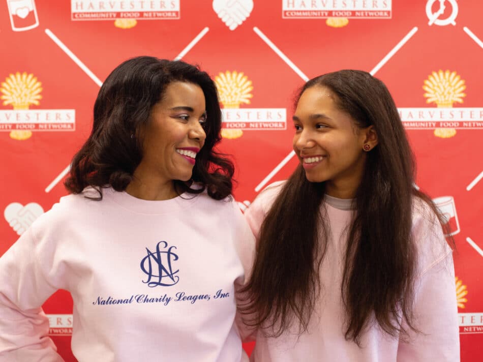 Mother looking at daughter both in pink shirts in front of step and repeat.