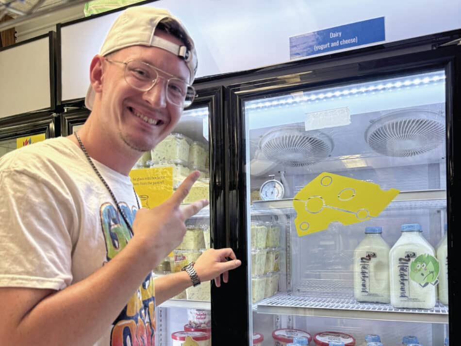 Gavin Cranor near a refrigerator holding up two fingers in greeting with a baseball hat on backwards.